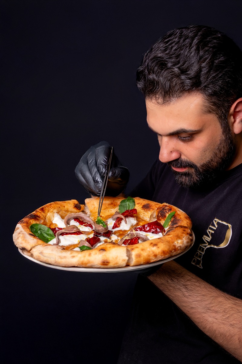 Pizzaiolo di Premiata Forneria rifinisce con pinzetta una pizza dal cornicione alto: burrata, peperoni, alici, basilico